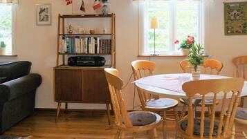 A cozy room with a wooden cabinet, bookshelves, a dining table with chairs, and a window with curtains.