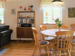 A cozy room with a wooden cabinet, bookshelves, a dining table with chairs, and a window with curtains.