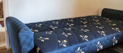 A bed with a floral pattern, a dark blue headboard, and a wooden floor.