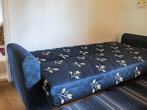 Un lit orné d’un motif floral, avec une tête de lit bleu foncé et un plancher en bois.