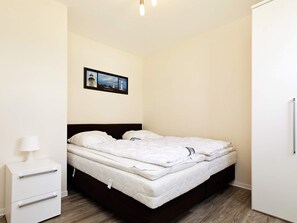 A hotel room with a bed, a nightstand, a lamp, and a wardrobe. - Holiday Home in Grossenbrode (Grossenbrode)