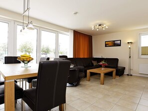 A modern living room with a dining table, leather sofa, and a floor lamp. - Holiday Home in Grossenbrode (Grossenbrode)