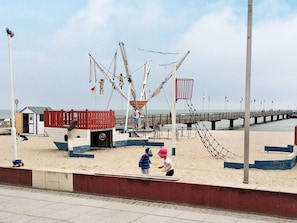 A beach with a swing set, a small building, and a pier extending into the water. - Holiday Home in Grossenbrode (Grossenbrode)