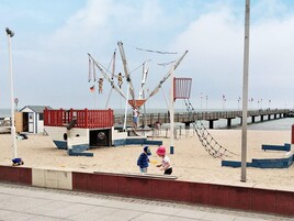 Una playa con un columpio, un edificio pequeño y un muelle que se adentra en el agua.