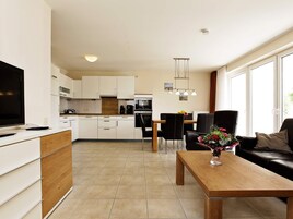 Una cocina moderna con armarios blancos, una zona de comedor con mesa y sillas de madera, y una sala de estar con sofá y mesa de centro.