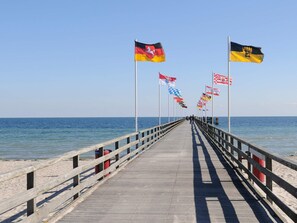 A wooden pier extending into the sea with multiple flags on poles.