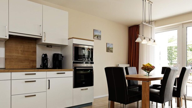 A modern kitchen with white cabinets, a wooden countertop, and a dining area with a table and chairs. - Holiday Home in Grossenbrode (Grossenbrode)