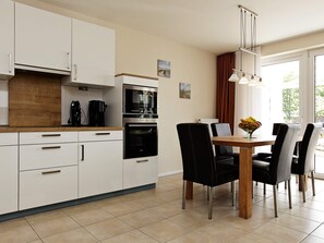 Een moderne keuken met witte kastjes, een houten aanrechtblad en een eethoek met een tafel en stoelen.
