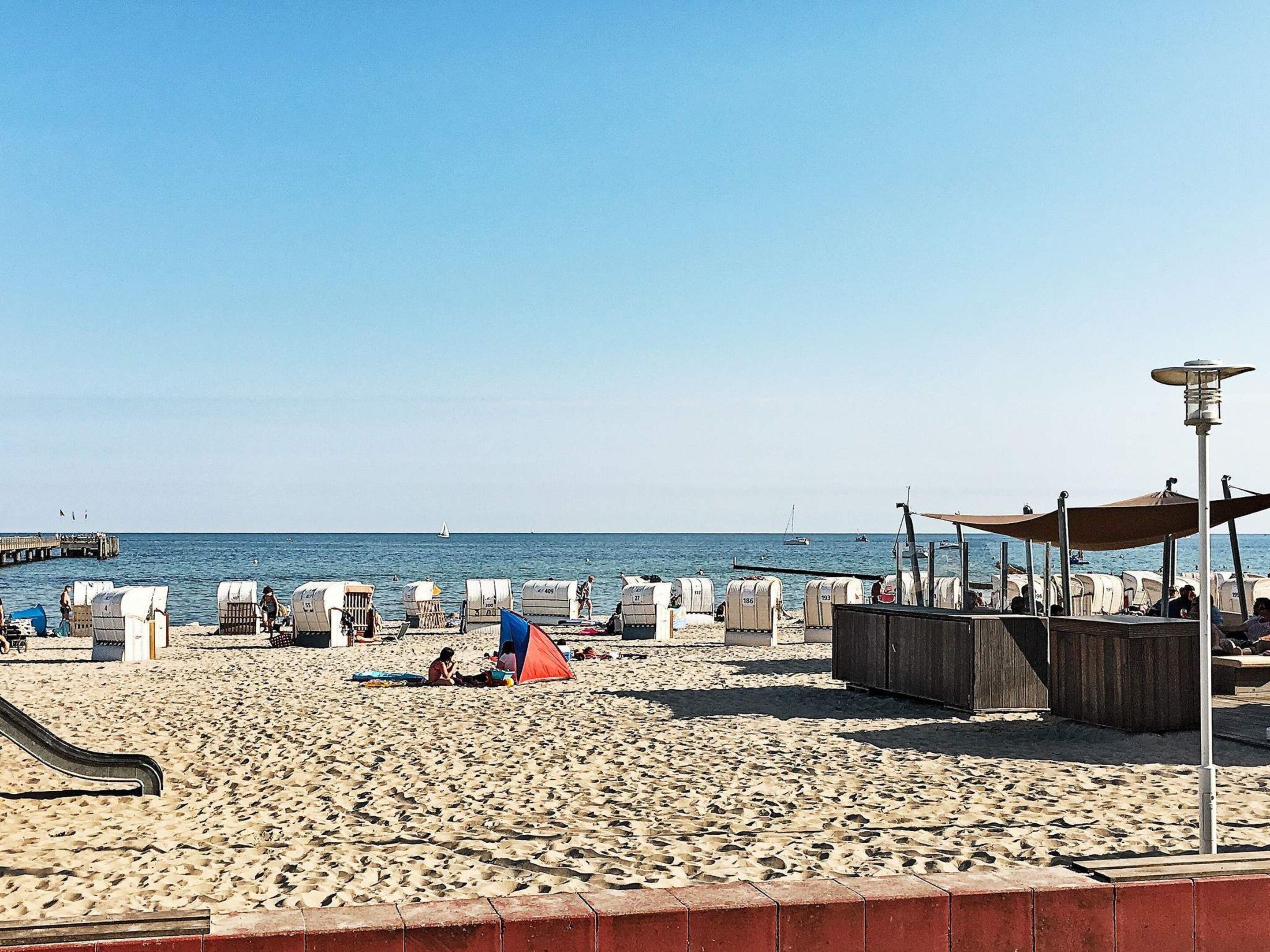 A beach with a pier, tents, and a lifeguard stand.