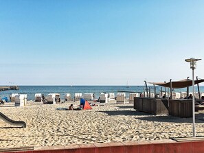 A beach with a pier, tents, and a lifeguard stand. - Holiday Home in Grossenbrode (Grossenbrode)
