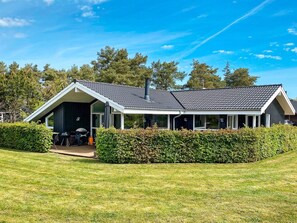 A modern house with a covered patio, a chimney, and a well-maintained lawn. - 5 Star Holiday Home in Hals (Hals)