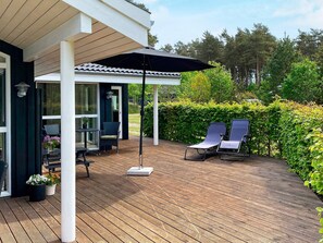 A wooden deck with two lounge chairs and a table, a covered seating area, and a hedge in the background. - 5 Star Holiday Home in Hals (Hals)