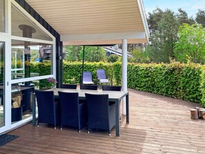 An outdoor patio with a table and chairs, a covered seating area, and a view of a hedge and trees. - 5 Star Holiday Home in Hals (Hals)