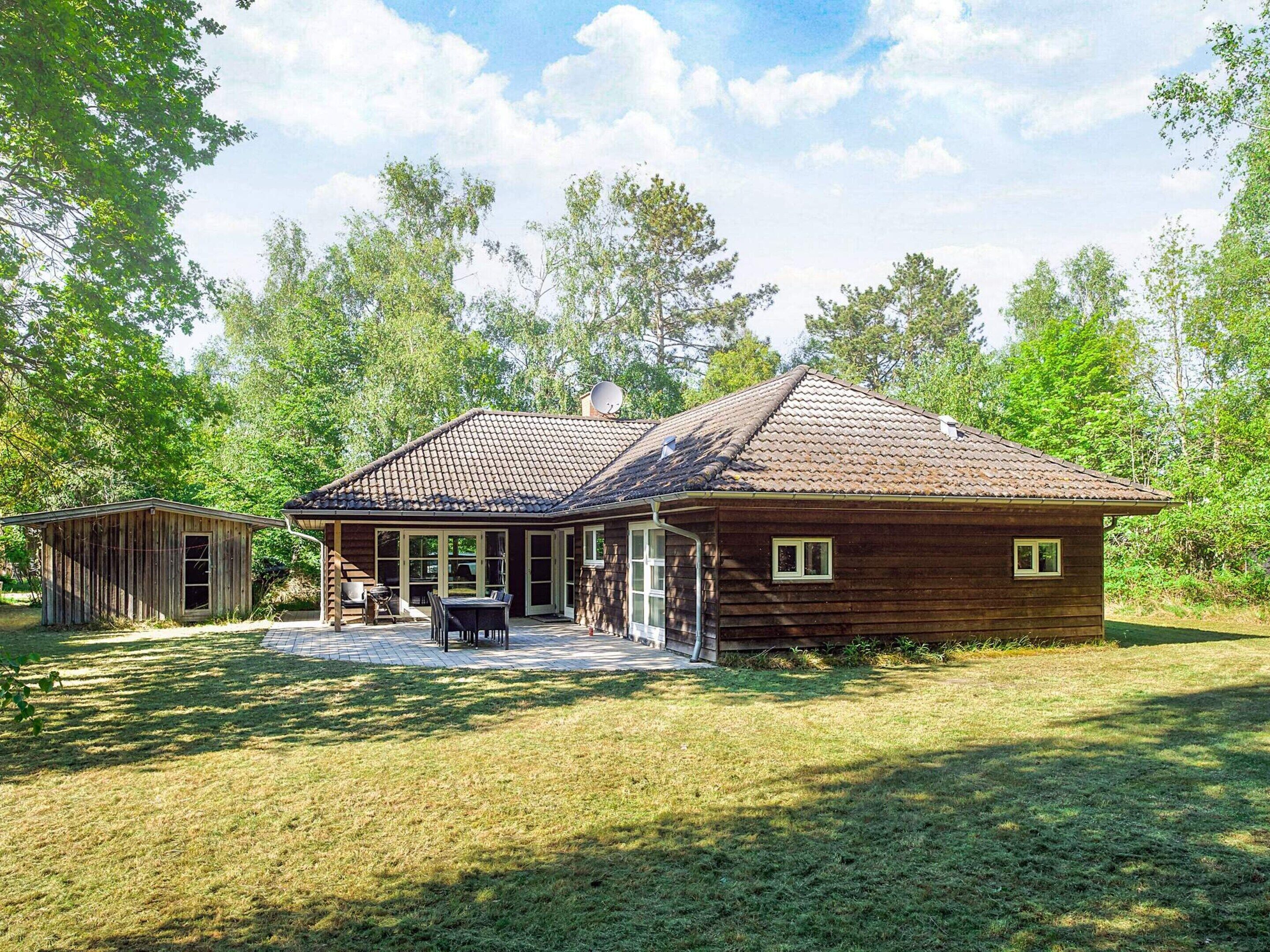 A rustic wooden cabin with a tiled roof, a covered patio, and a small adjacent shed.