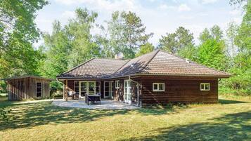 A rustic wooden cabin with a tiled roof, a covered patio, and a small adjacent shed.