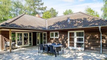A wooden house with a tiled roof, a patio with a table and chairs, and a satellite dish.