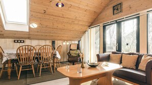 Un intérieur de chalet chaleureux avec un coin repas en bois, un canapé et de grandes fenêtres.