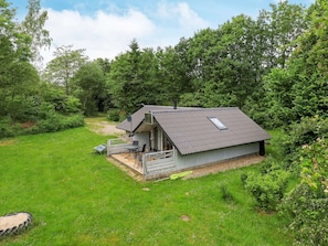 Une petite cabane à un seul étage, dotée d’un toit en pente, d’une terrasse avec des meubles d’extérieur, et entourée d’une végétation luxuriante.