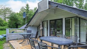 Une terrasse extérieure couverte, équipée d’une table et de chaises, d’une antenne parabolique et offrant une vue sur la végétation environnante.