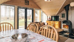 L’intérieur chaleureux d’un chalet avec un plafond en bois, une cheminée, une table à manger et un téléviseur.
