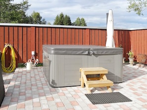 A hot tub with a wooden bench and a small table, a hose, and a water pump on a brick patio. - 4 Person Holiday Home in Rattvik (Rattvik)