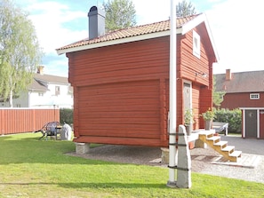 A red wooden building with a chimney, a staircase, and a small garden area with a bench and chairs. - 4 Person Holiday Home in Rattvik (Rattvik)