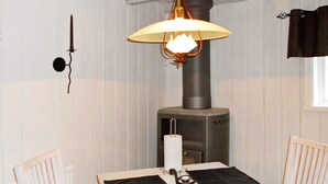 A room with a white table, two chairs, a wall-mounted lamp, and a wood-burning stove. - 4 Person Holiday Home in Rattvik (Rattvik)