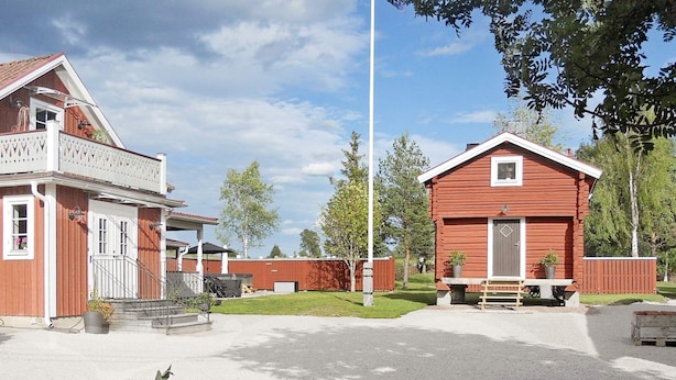 A two-story building with a porch and a covered area, surrounded by a fence and greenery. - 4 Person Holiday Home in Rattvik (Rattvik)