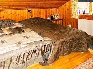 A bed with a quilt and pillows, a wooden floor, a radiator, and a small table with bottles and a plate. - 4 Person Holiday Home in Rattvik (Rattvik)