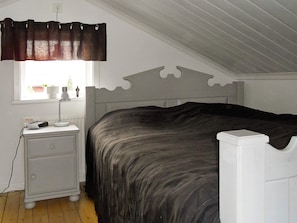 A bedroom with a bed, a bedside table, a lamp, a window with curtains, and a radiator. - 4 Person Holiday Home in Rattvik (Rattvik)
