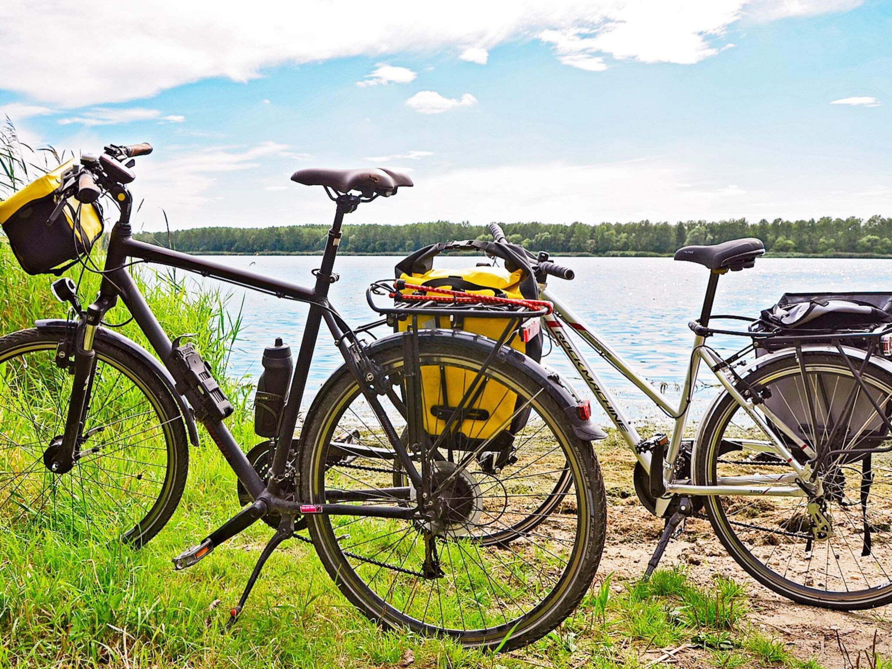 A bicycle with a yellow basket and a black bag, parked by a lake with a clear sky.