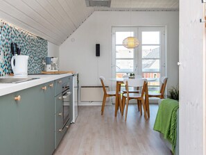 A modern kitchen with a dining area, featuring a large window, wooden chairs, and a green towel.