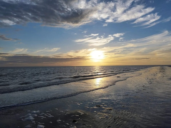 Une plage où le soleil se couche à l’horizon, et où les vagues viennent doucement lécher le rivage.