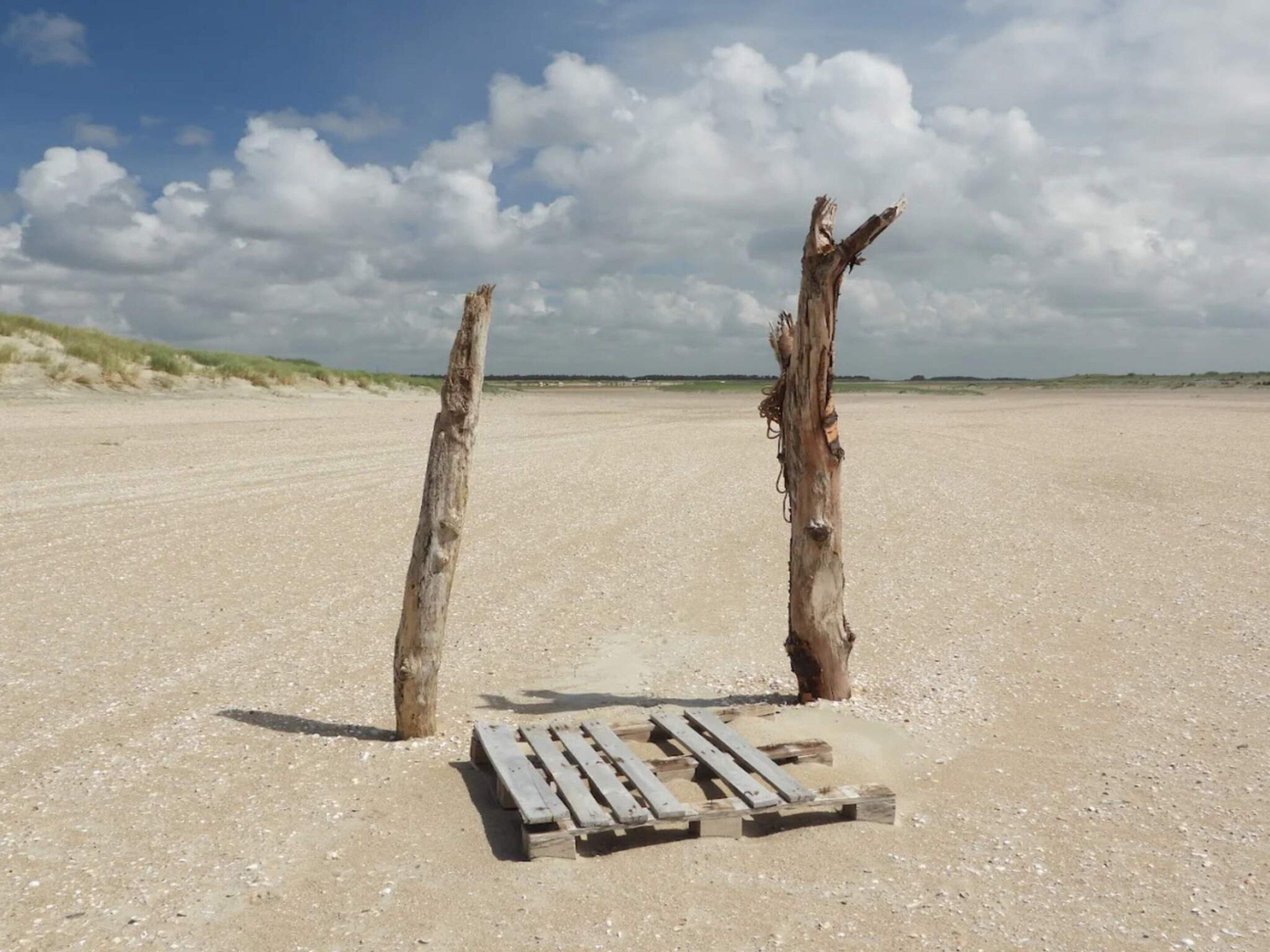 Two wooden posts in a sandy area with a wooden bench in front.