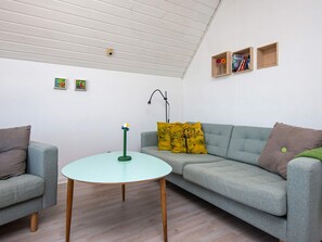 A living room with a grey sofa, a round table, and a lamp. There are picture frames on the wall and a small shelf with books. - 5 Person Holiday Home in Romo-by Traum (Rømø)