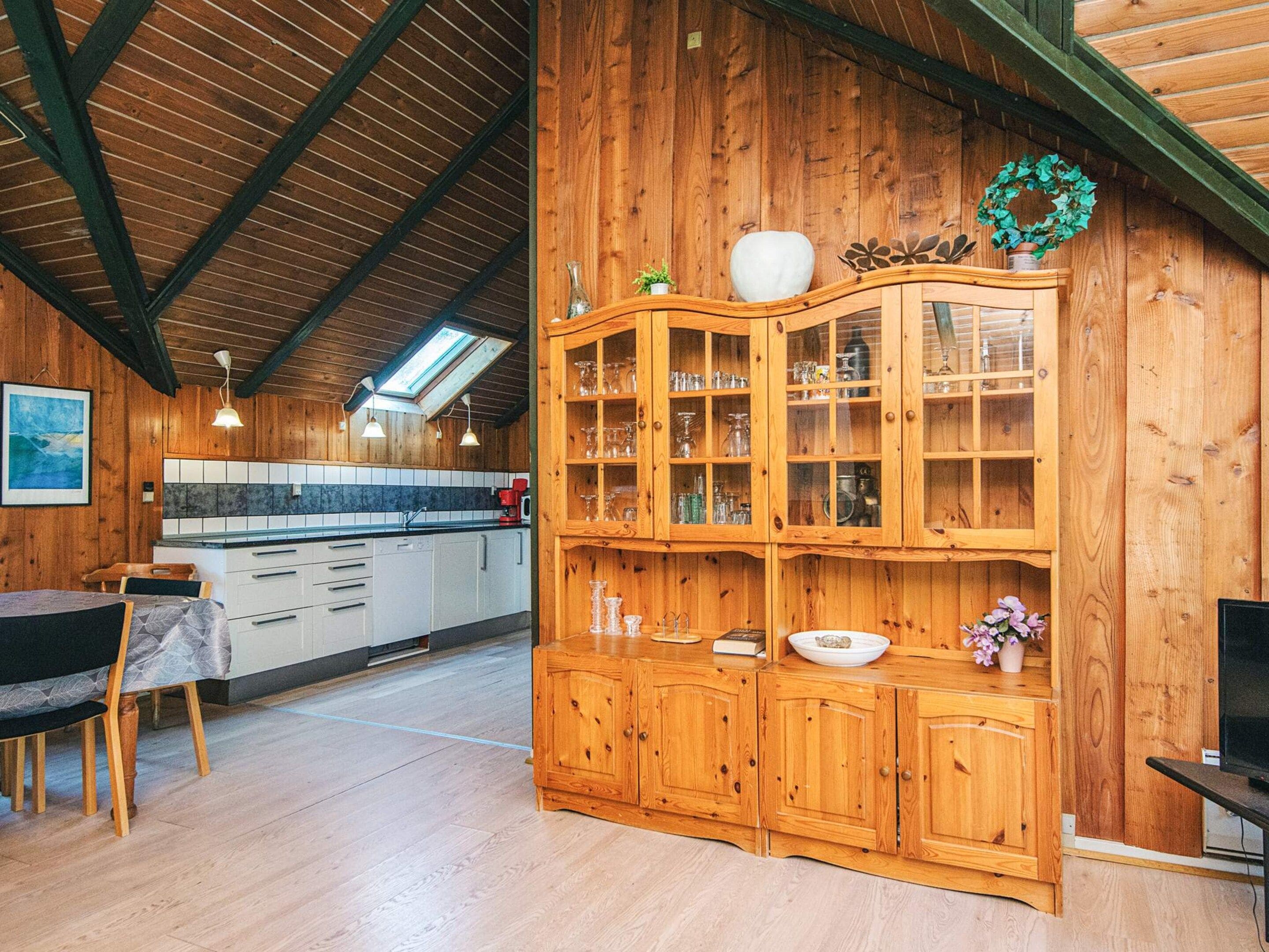 A wooden interior with a kitchen area, a dining table, and a built-in cabinet with glass doors.