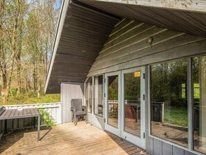 Eine überdachte Terrasse mit Stuhl, Tisch und einer Glastür, die zu einem weiteren Terrassenbereich führt.