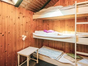 Ein Schlafraum mit Etagenbetten, Holzwänden, einem kleinen Tisch und einem Einzelbett mit Kissen und Decke.