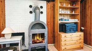 A room with a wood-burning stove, a wooden cabinet with shelves, and a table with a lamp. - 7 Person Holiday Home in Toftlund (Toftlund)