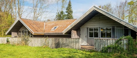 Una casa de un piso con techo inclinado, cerca de madera y jardín cubierto de césped.