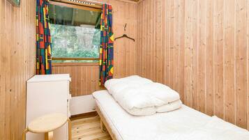Une petite chambre avec un lit simple, un plancher en bois, un bureau et une fenêtre avec des rideaux.