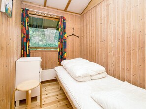 A small, single-room cabin with a bed, a small table, and a window with curtains. - 4 Person Holiday Home in Skibby (Skibby)