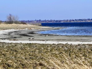 A coastal landscape with a sandy beach, a body of water, and a distant shoreline with buildings. - 4 Person Holiday Home in Skibby (Skibby)