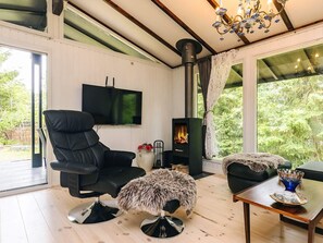 A modern living room with a black leather chair, a fluffy ottoman, a wooden coffee table, a fireplace, and a TV mounted on the wall. - 4 Person Holiday Home in Skibby (Skibby)