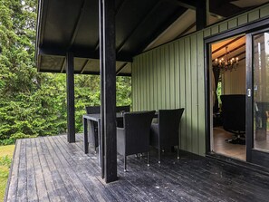 A covered outdoor area with a table and chairs, a wooden deck, and a view of a forested area. - 4 Person Holiday Home in Skibby (Skibby)