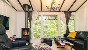 A cozy living room with a fireplace, leather furniture, a chandelier, and large windows with curtains.
