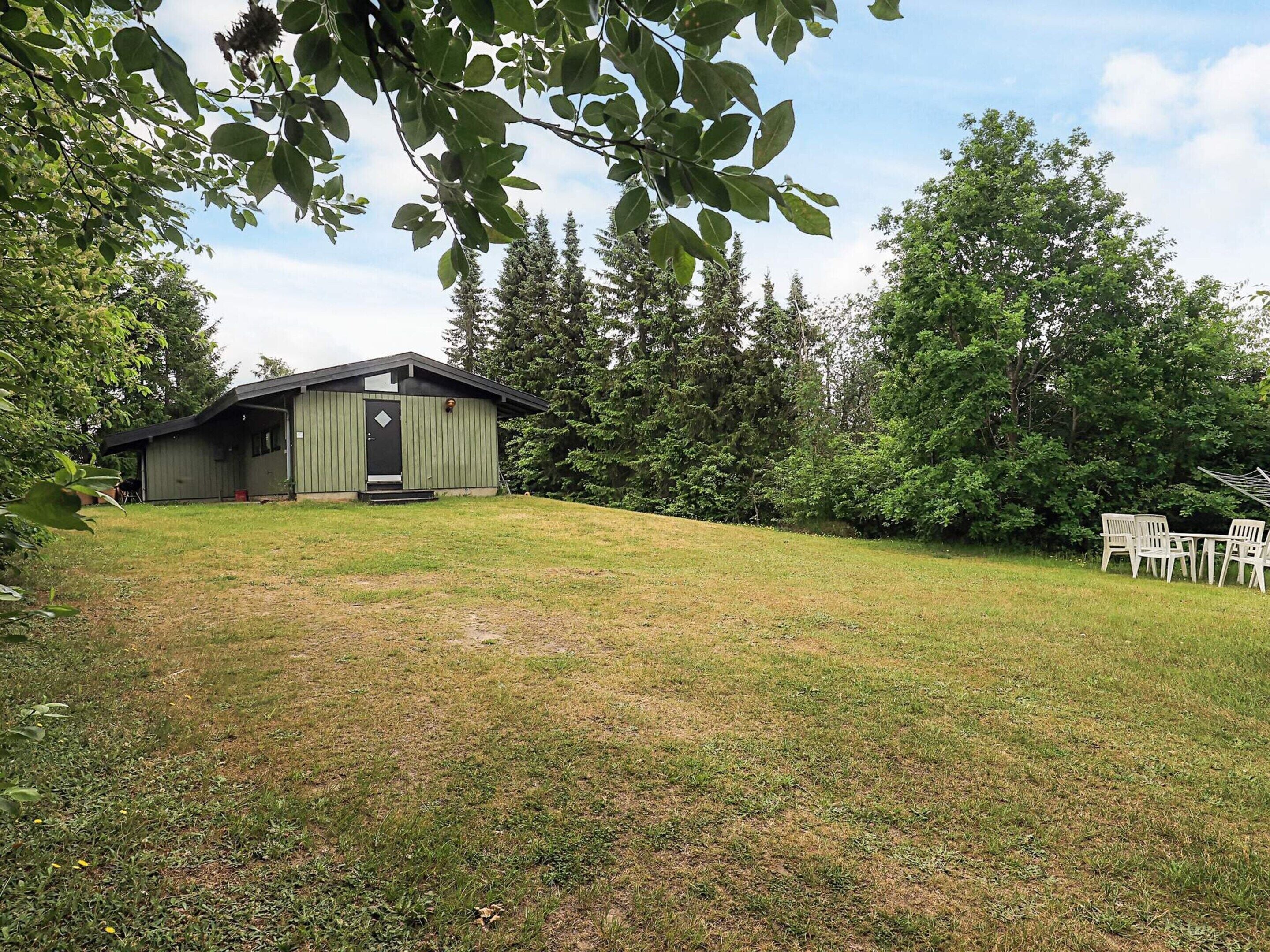 A single-story building with a dark roof and light walls, surrounded by a grassy area and trees.
