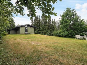 A single-story building with a dark roof and light walls, surrounded by a grassy area and trees. - 4 Person Holiday Home in Skibby (Skibby)