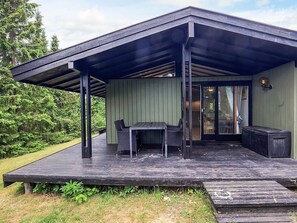 A covered outdoor area with a table and chairs, a bench, and a trash can. - 4 Person Holiday Home in Skibby (Skibby)