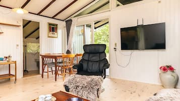 A room with a wooden dining table, a black chair, a television, and a large window.